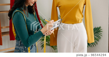 The designer is measuring the shirt fashion working on her designs in the studio.. 96544294