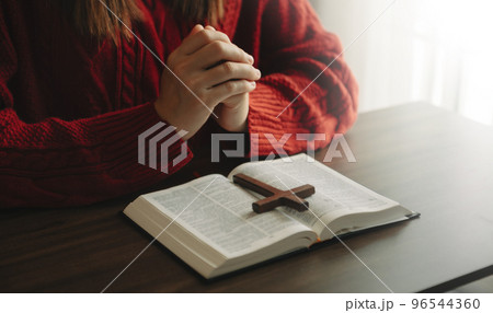 Hands together in prayer to God along with the bible In the Christian concept and religion, woman pray in the Bible on the wooden table. 96544360
