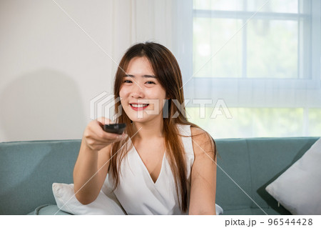 Beautiful female person look movie holding remote controller watching television, woman smiling sit relaxing watch TV hold remote control looking news on sofa in living room, entertainment lifestyles 96544428