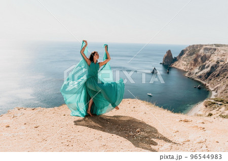 Side view a Young beautiful sensual woman with black hair in a long mint dress posing on a beach with calm sea bokeh lights on sunny day. Girl on the nature on blue sky background. Fashion photo 96544983