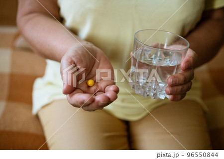 Mature woman with a glass of water holds a pill in her hand 96550844