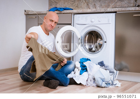 tired man sits with laundry at the washing machine tired man sits with laundry at the washing machine 96551071