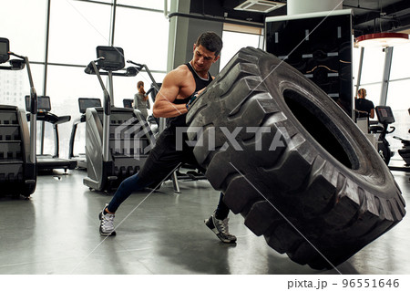 Muscular fitness man moving large tire in gym center, concept lifting, workout training. 96551646