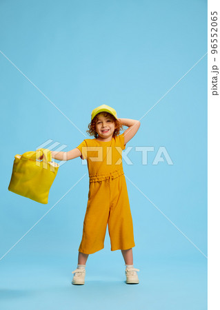 Portrait of cute little girl, child with curly red hair posing isolated over blue background. Stylish yellow outfit Portrait of cute little girl, child with curly red hair posing isolated over blue background. Stylish yellow outfit 96552065