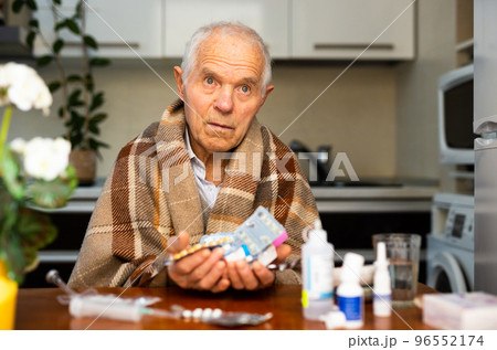 gray haired elderly man with handful of different medications in hand at home 96552174