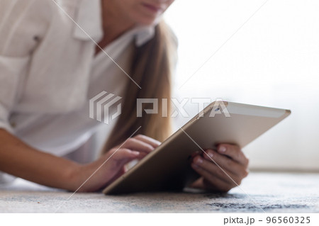 Young woman laying on the carpet at home and using a tablet. Closeup. Selective focus. 96560325