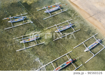 A top-down view of a group of traditional Balinese fishing boats moored to shore. Boats with additional beams on the sides against the backdrop of green ocean water in shallow water 96560326