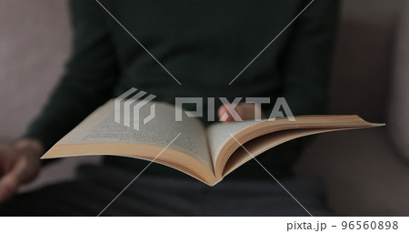 Man is lifestyle sitting on couch in cozy room reading favorite book. Man opens the book and turns the pages of the book. 96560898