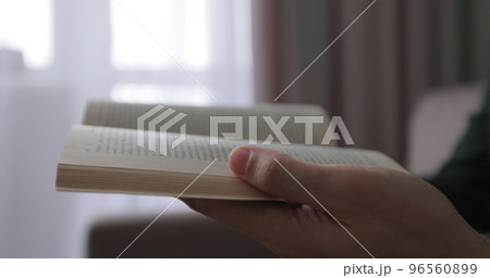 Young man read book while sitting on a sofa at home. Close up at book in hands. 96560899