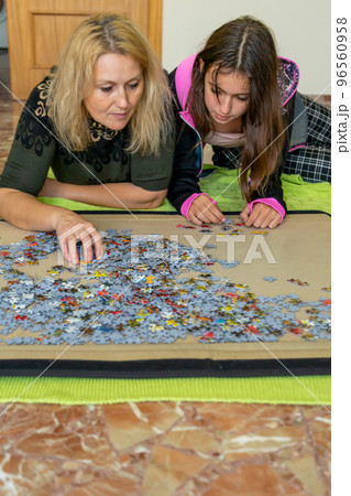 Mother and daughter lying on the floor doing a puzzle together while having a nice time on a girls night out. 96560958