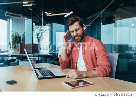 Sick businessman at work with laptop, man in red shirt and glasses has severe headache and flashes, overtired working inside office. 96561818