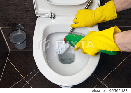 Cleaner in yellow rubber gloves cleans the toilet bowl with a brush and disinfectant 96562483