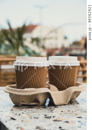 Two paper cups with lid for tea to go. Coffee take away on the table. Take-out coffees with brown paper cup holder. Brown safety cardboard collars. Cardboard tray Two paper cups with lid for tea to go. Coffee take away on the table. Take-out coffees with brown paper cup holder. Brown safety cardboard collars. Cardboard tray 96562921