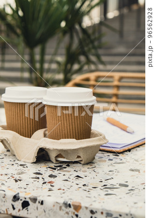 Two paper cups with lid for tea to go. Coffee take away on the table. Take-out coffees with brown paper cup holder. Brown safety cardboard collars. Cardboard tray 96562928