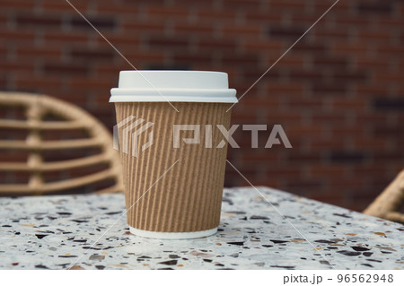 Eco recycling paper cup with coffee or tea on craft paper on table in beach cafe. Take away coffee to go. Copy space for text. Disposable 96562948