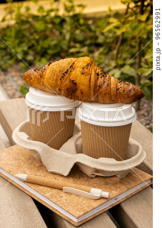 Fresh baked chocolate croissant on Two paper cups with lid for tea to go. Empty paper notebook. Freelancer's place of work. Study and work online. Remote business education. Making plans for next week 96562991