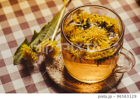 Dandelion flower healthy tea in glass cup on table. Herbal medicine Delicious tisane tea from with fresh yellow blossom dandelion flowers inside tea cup. Green clearing infusion Wildflowers Eco Dandelion flower healthy tea in glass cup on table. Herbal medicine Delicious tisane tea from with fresh yellow blossom dandelion flowers inside tea cup. Green clearing infusion Wildflowers Eco 96563129