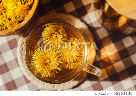 Dandelion flower healthy tea in glass teapot and glass cup on table. Delicious herbal Hot tea from fresh dandelion flowers at home at summer day. Green clearing. Bouquet of dandelions petals Dandelion flower healthy tea in glass teapot and glass cup on table. Delicious herbal Hot tea from fresh dandelion flowers at home at summer day. Green clearing. Bouquet of dandelions petals 96563130