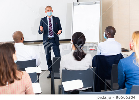 caucasian male businessman in mask gives advice to manager in meet room 96565204