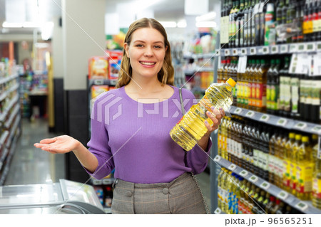 Smiling young woman choosing the different oil in the modern supermarket Smiling young woman choosing the different oil in the modern supermarket 96565251