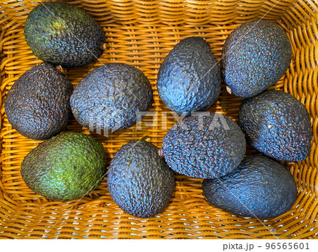 A basket full of avocados over a wooden surface seen from above. 96565601