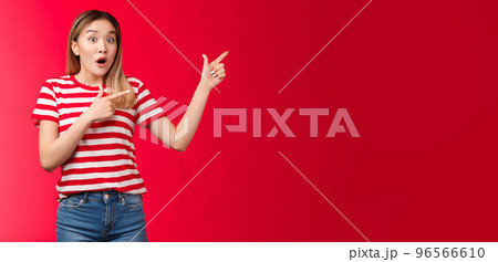 Surprised impressed attractive modern asian girl blond haircut open mouth gasping astonished, pointing right, show fingers impressive stunning promo new clothes collection look camera enthusiastic 96566610