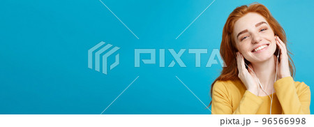 Lifestyle concept - Portrait of cheerful happy ginger red hair girl enjoy listening to music with headphones joyful smiling to camera. Isolated on Blue Pastel Background. Copy space. 96566998