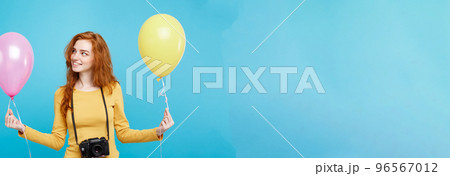 Lifestyle and Party concept - Close up Portrait young beautiful attractive ginger red hair girl with colorful balloon and vintage camera. Blue Pastel Background. Copy space. Lifestyle and Party concept - Close up Portrait young beautiful attractive ginger red hair girl with colorful balloon and vintage camera. Blue Pastel Background. Copy space. 96567012