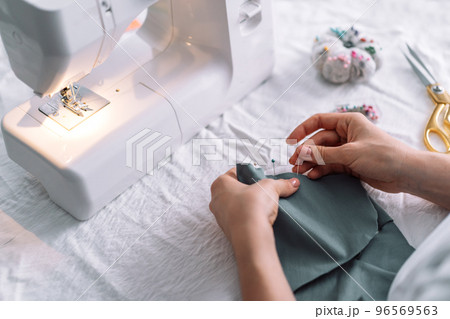 Lady fixes fabric with needles in front of a sewing machine 96569563