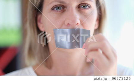 Young woman unsticking duct tape on mouth Young woman unsticking duct tape on mouth 96575129