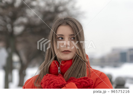 Close-up portrait of beautiful girl in red jacket warming hand in red knitted mittens. Young woman in warm clothes outdoors in winter 96575216