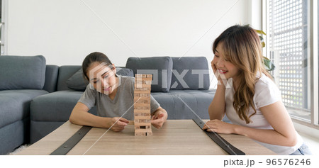 Two asian woman enjoy playing  wooden blocks game in the living room. Players take turns removing one block at a time from a tower constructed of 54 blocks. 96576246