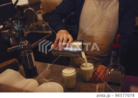 Barista pours milk in to glasses on wooden table in cafe. Making tasty coffee drink with milk 96577078