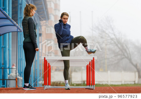 Two young women doing hurdle athletics training on the track Two young women doing hurdle athletics training on the track 96577923