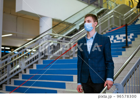 Young caucasian man wearing a medical mask on the steps in a shopping mall 96578300