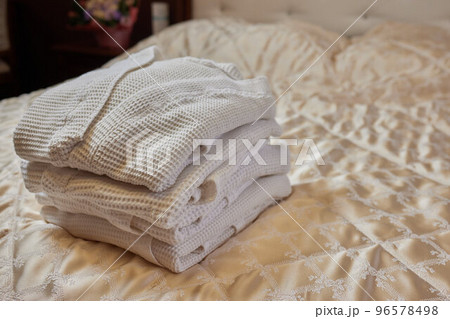 A beautiful white folded robe lies on the edge of the bed with a gray veil in a cozy and expensive hotel room. 96578498