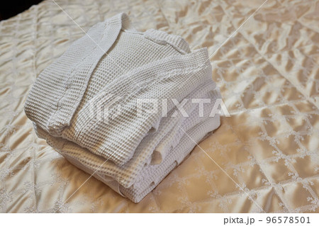 A beautiful white folded robe lies on the edge of the bed with a gray veil in a cozy and expensive hotel room. 96578501