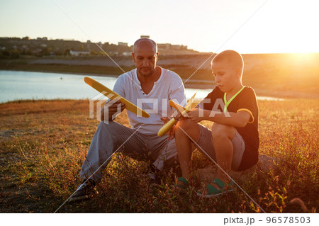 dad and son play the plane at sunset 96578503