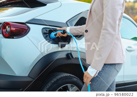 Close-up of woman holding power supply cable from her electric car, charging it in home, sustainable and economic transportation concept. 96580022