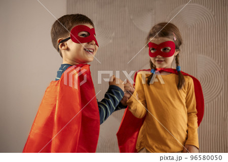 Portrait of a team of two young superheroes, brother and sister, over beige background 96580050