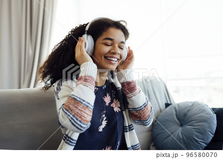 African millennial woman in orange sweater wearing wireless headphones, 96580070