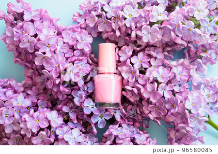 Pink nail polish small mini glass bottle and lilac flowers on blue background. Professional manicure concept. Mockup, front view. Pink nail polish small mini glass bottle and lilac flowers on blue background. Professional manicure concept. Mockup, front view. 96580085
