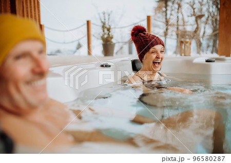 Senior couple in kintted cap enjoying together outdoor bathtub at their terrace during cold winter day. Senior couple in kintted cap enjoying together outdoor bathtub at their terrace during cold winter day. 96580287