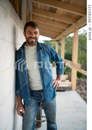 Happy mature man standing in front of his new house under construction, looking at camera. Happy mature man standing in front of his new house under construction, looking at camera. 96580335