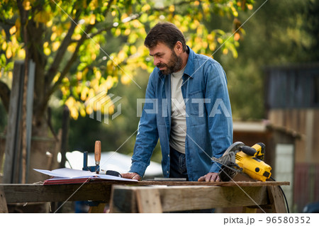 Handyman measuring a board, outside in garden. Handyman measuring a board, outside in garden. 96580352