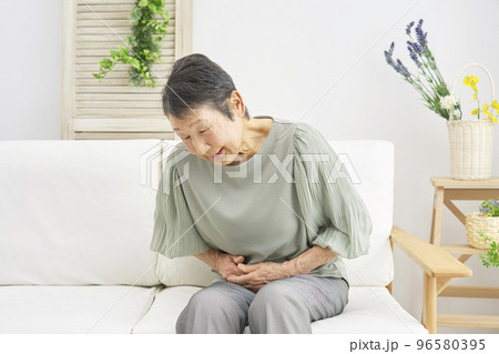 家で腹痛がする高齢者女性 96580395