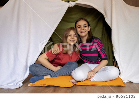 Happy young teen girls embracing indoors sitting in handmade wigwam. Happy young teen girls embracing indoors sitting in handmade wigwam. 96581105