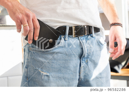 Man takes handmade black leather wallet out of pocket of his jeans pants. Advertising of craft leather accessories, close-up. Modern fashionable belt and male purse 96582286