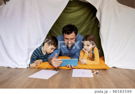 Happy father with little daughter and son drawing indoors in handmade wigwam Happy father with little daughter and son drawing indoors in handmade wigwam 96583599
