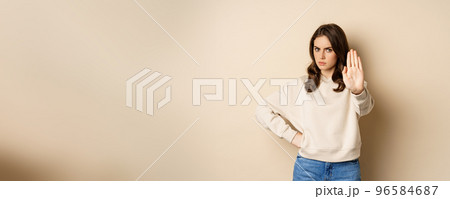 Stop. Serious and confident woman showing extended arm palm, prohibit, forbid smth, blocking something, standing over beige background 96584687